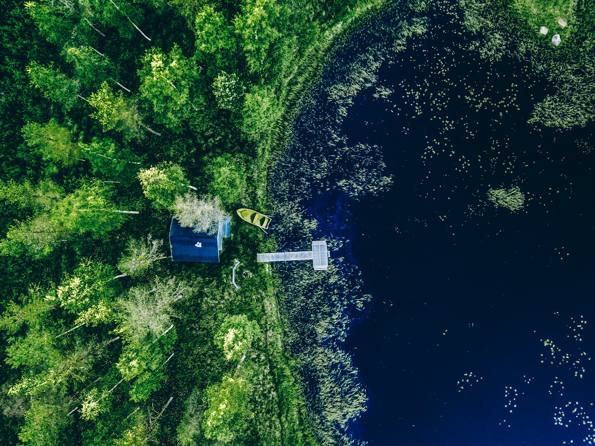 Aerial view of Sauna house by the lake shore. Wooden pier with fishing boat.